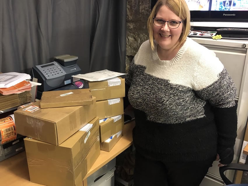 Imagen que muestra a Joanne junto a una pila de pedidos en sus cajas esperando su despacho